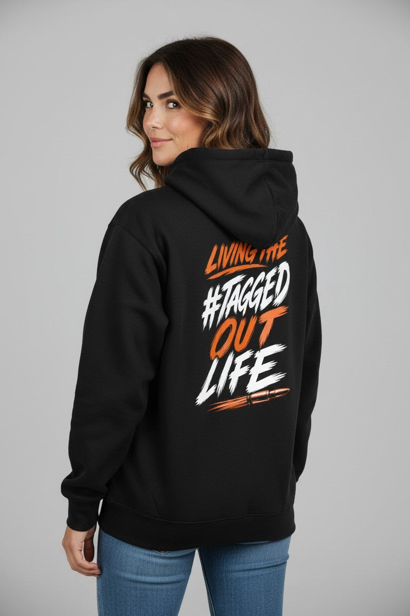 Woman wearing a black Tagged Out Life unisex hunting hoodie with orange and white rifle graphic on the back